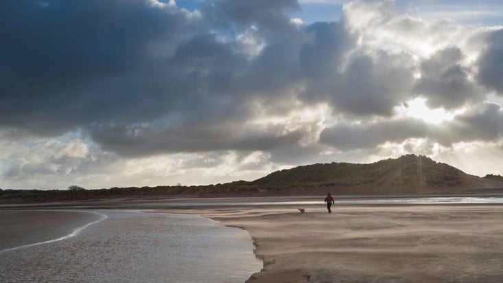 Visitor walking dog on the beach at Sandscale Haws National Nature Reserve, Lake District